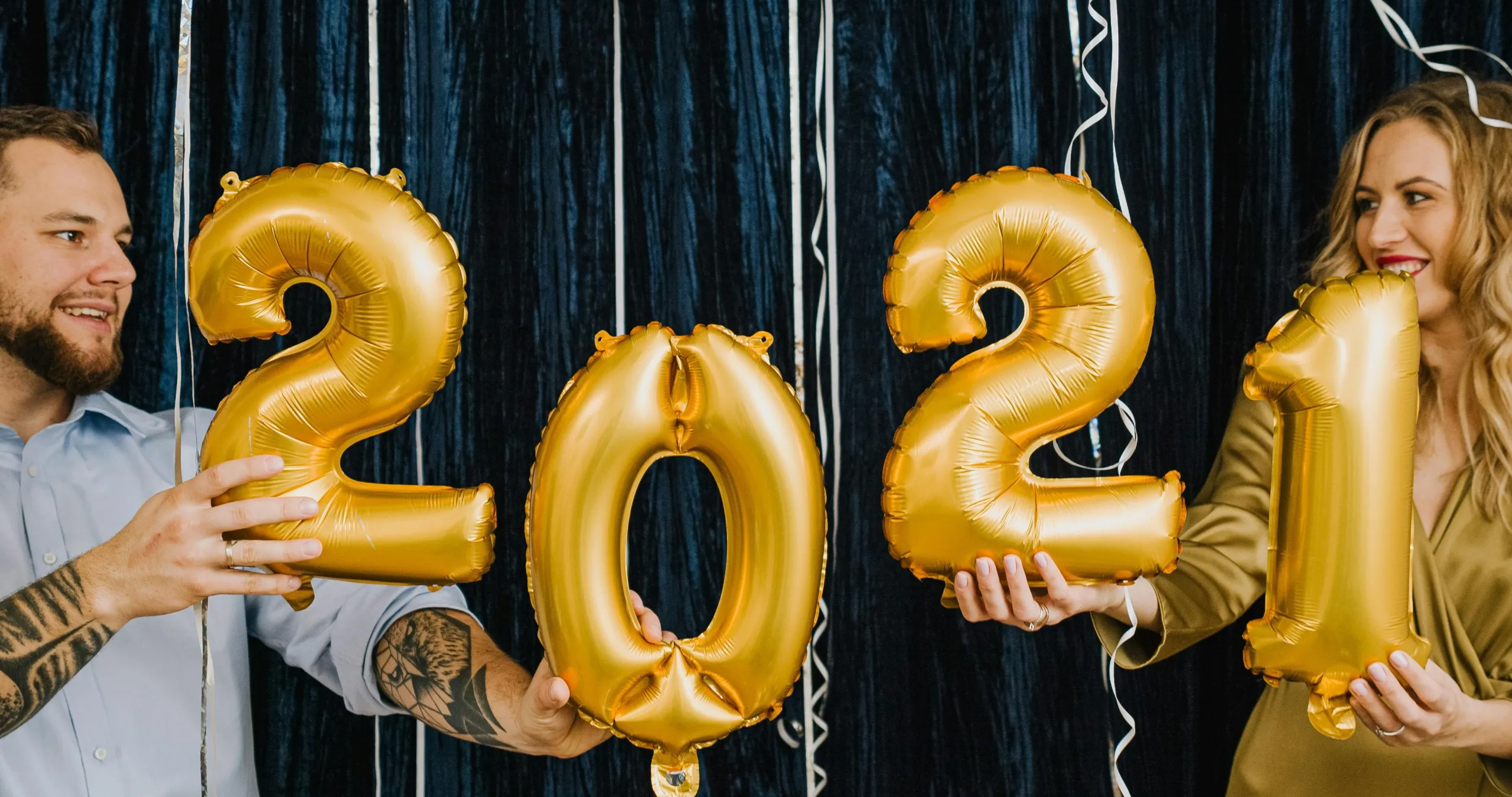 A photo of two people holding balloons reading 2021.