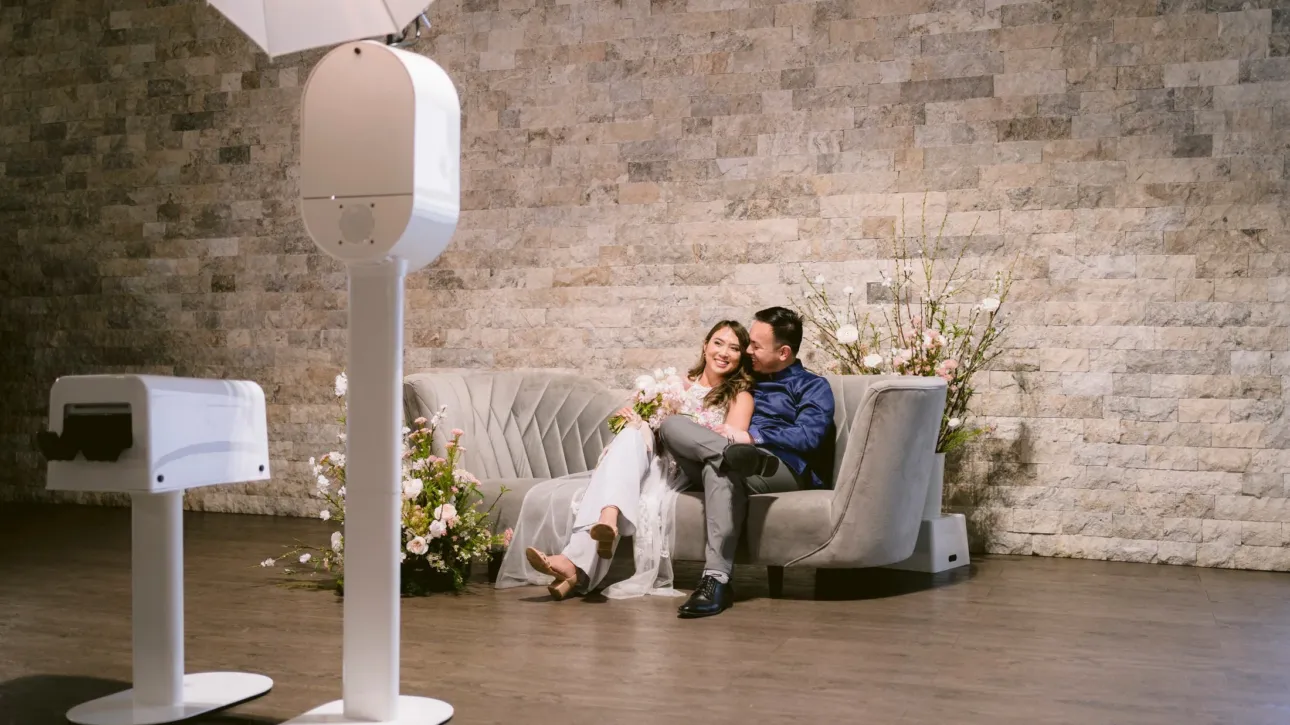 A photo booth taking a picture of a bridge and groom on a couch.