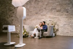 A photo booth taking a picture of a bridge and groom on a couch.