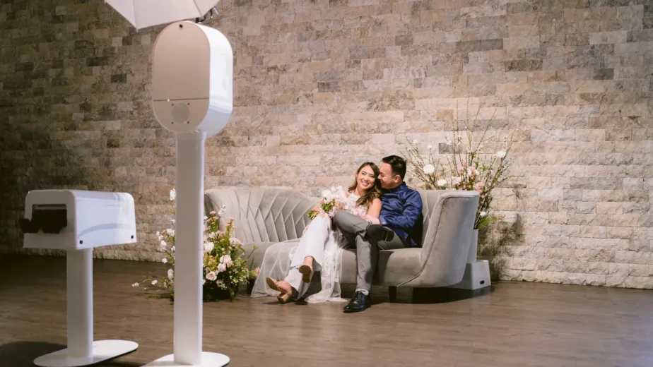 A photo booth taking a picture of a bridge and groom on a couch.