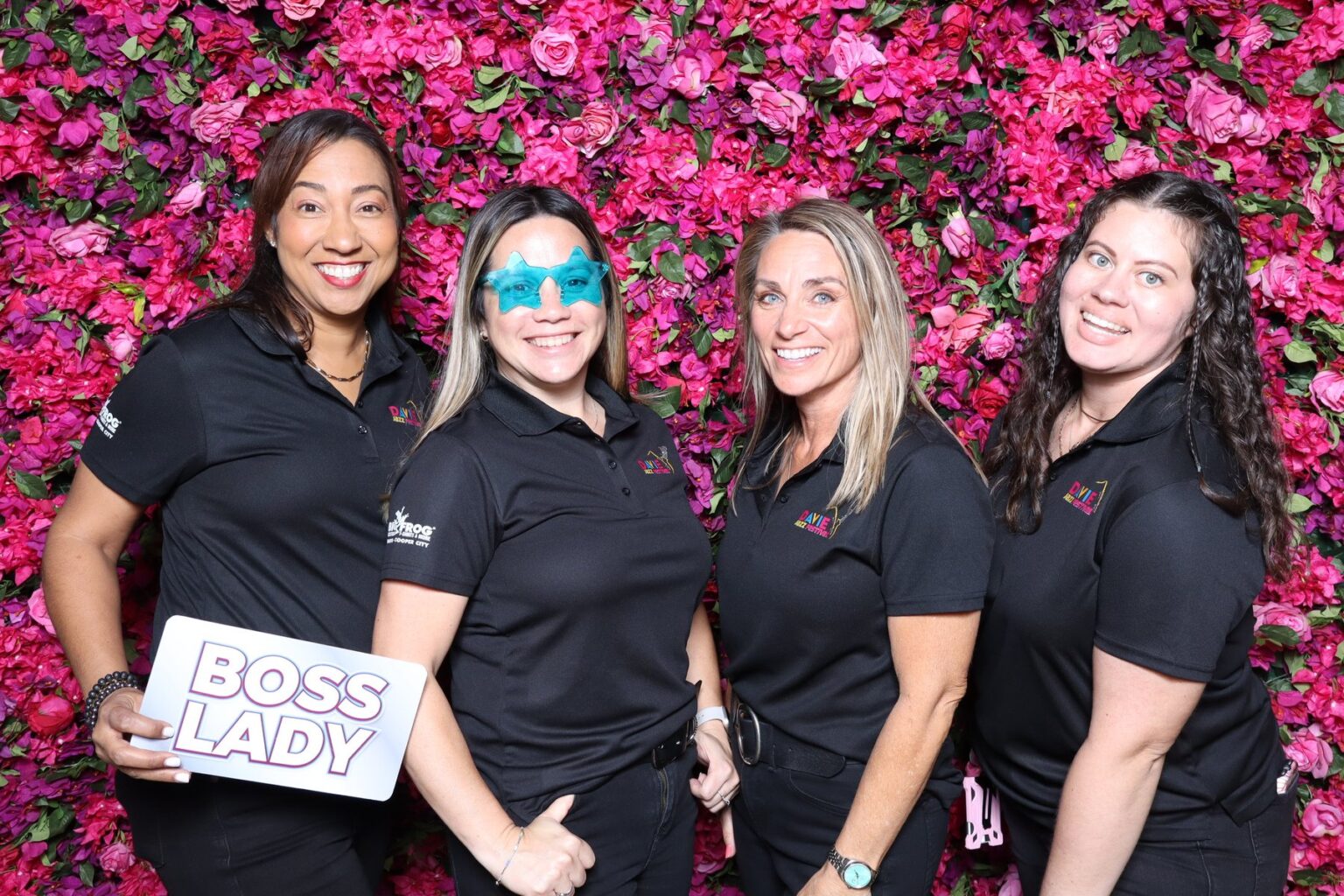 Four colleagues holding a Boss Lady prop at a pink flower wall photo booth