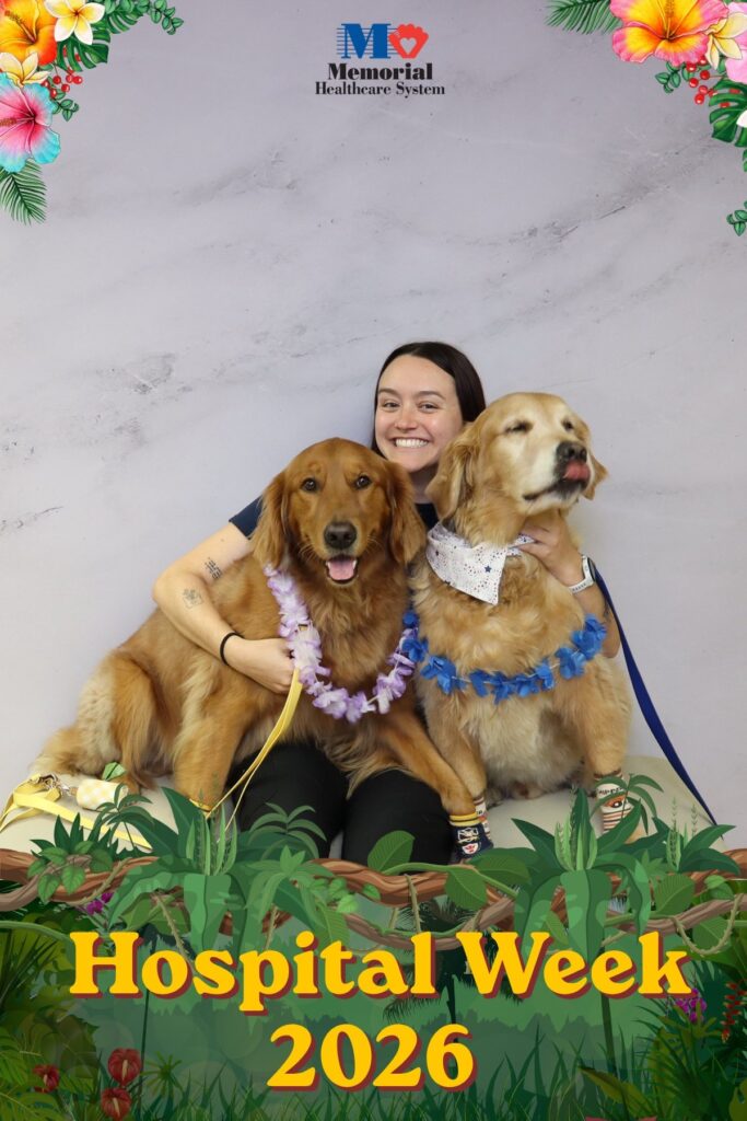 Hospital staff member sitting with two therapy dogs at a Hospital Week photo booth