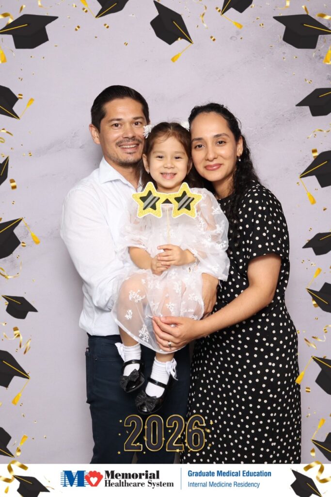 Family with a young child posing at a graduate medical education graduation photo booth