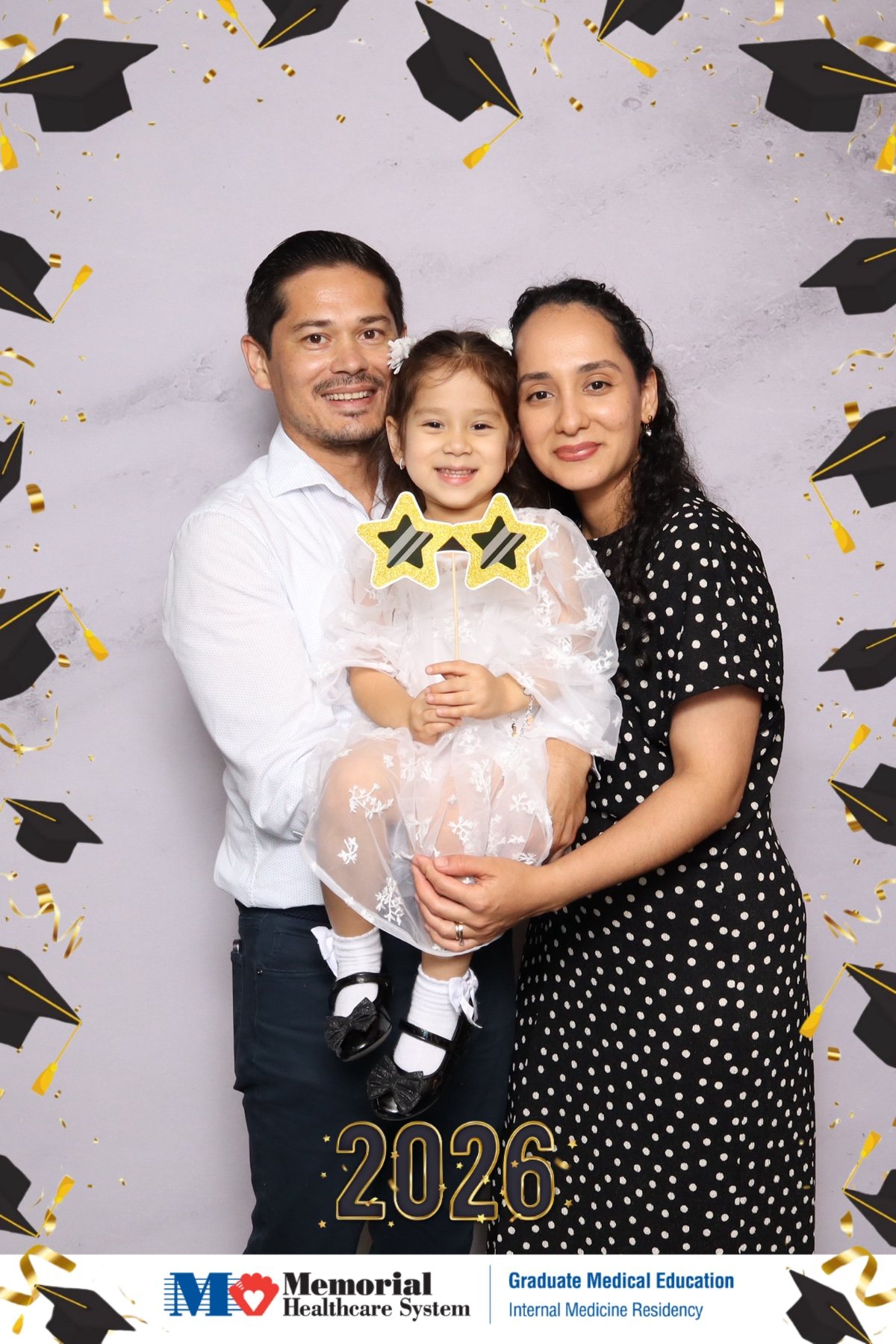 Family with a young child posing at a graduate medical education graduation photo booth