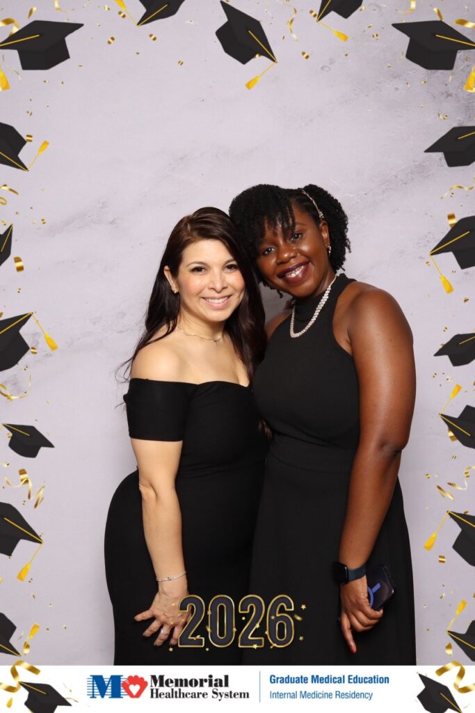 Two guests in black dresses at a medical residency graduation photo booth