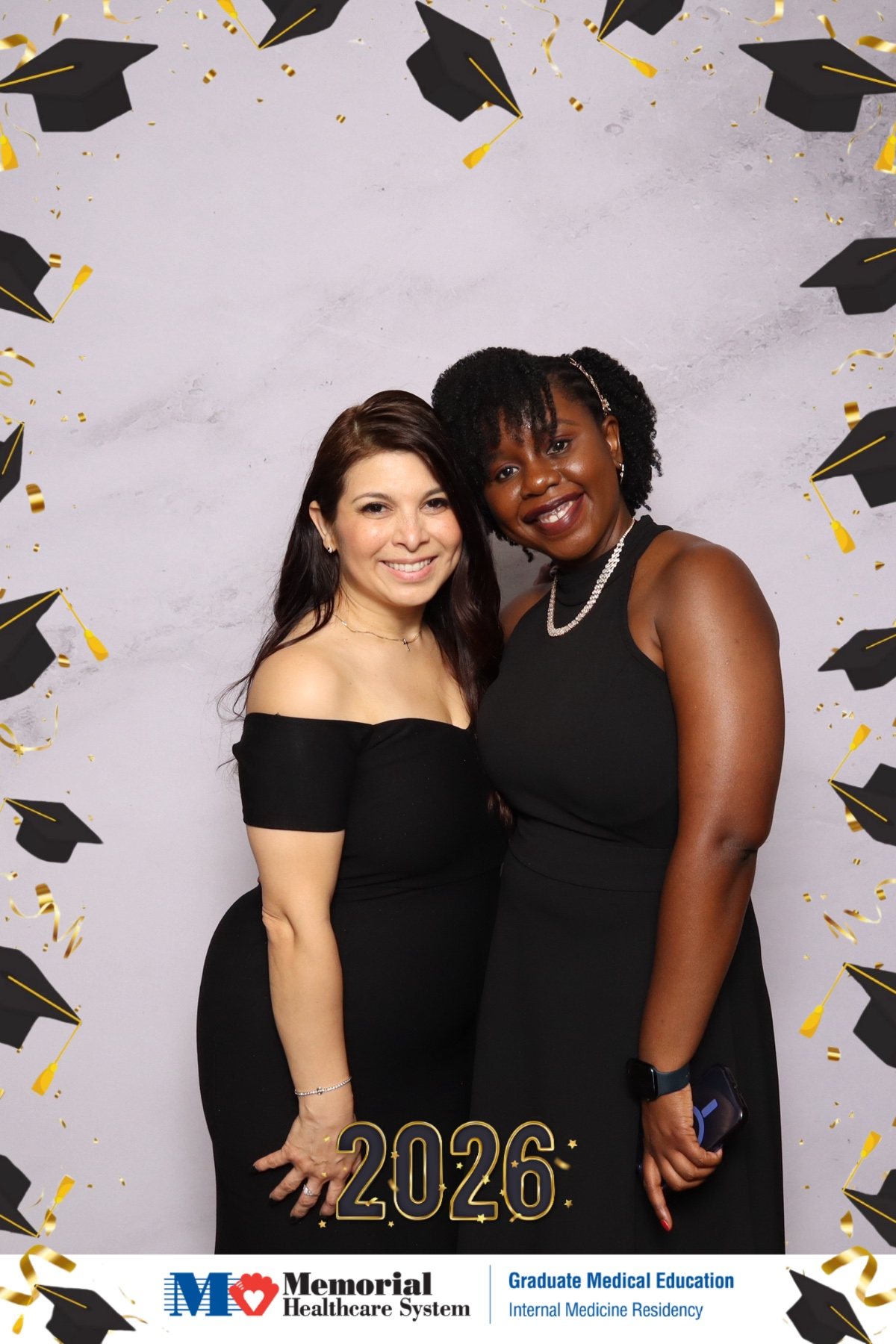 Two guests in black dresses at a medical residency graduation photo booth