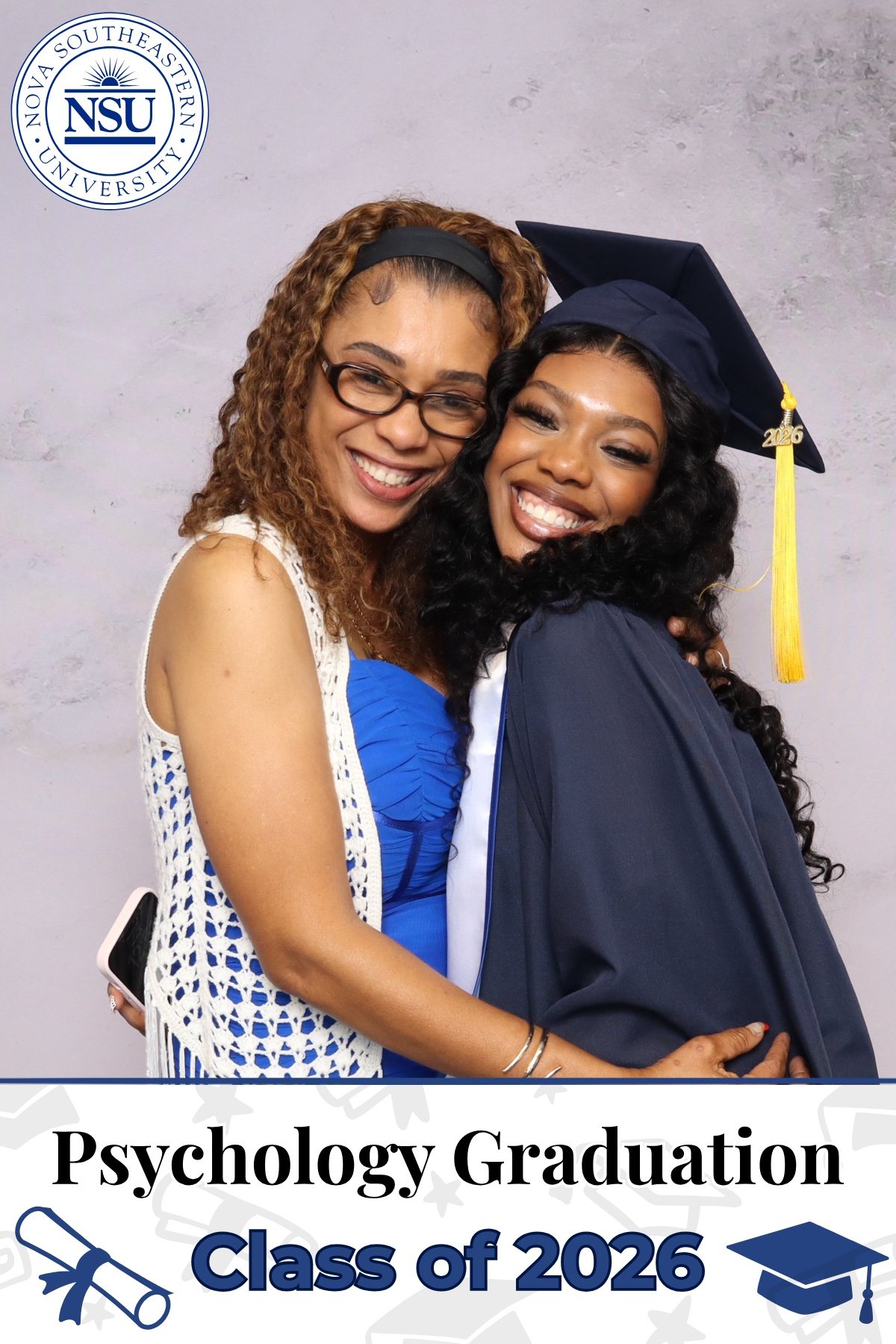 Graduate in cap and gown hugging a guest at a university graduation photo booth